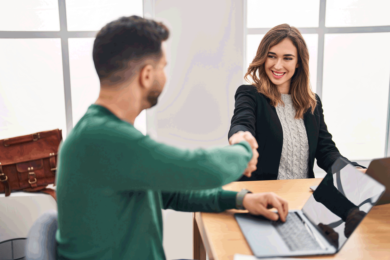 Person pointing at a laptop whilst speaking to another person, both sitting opposite sides of a desk